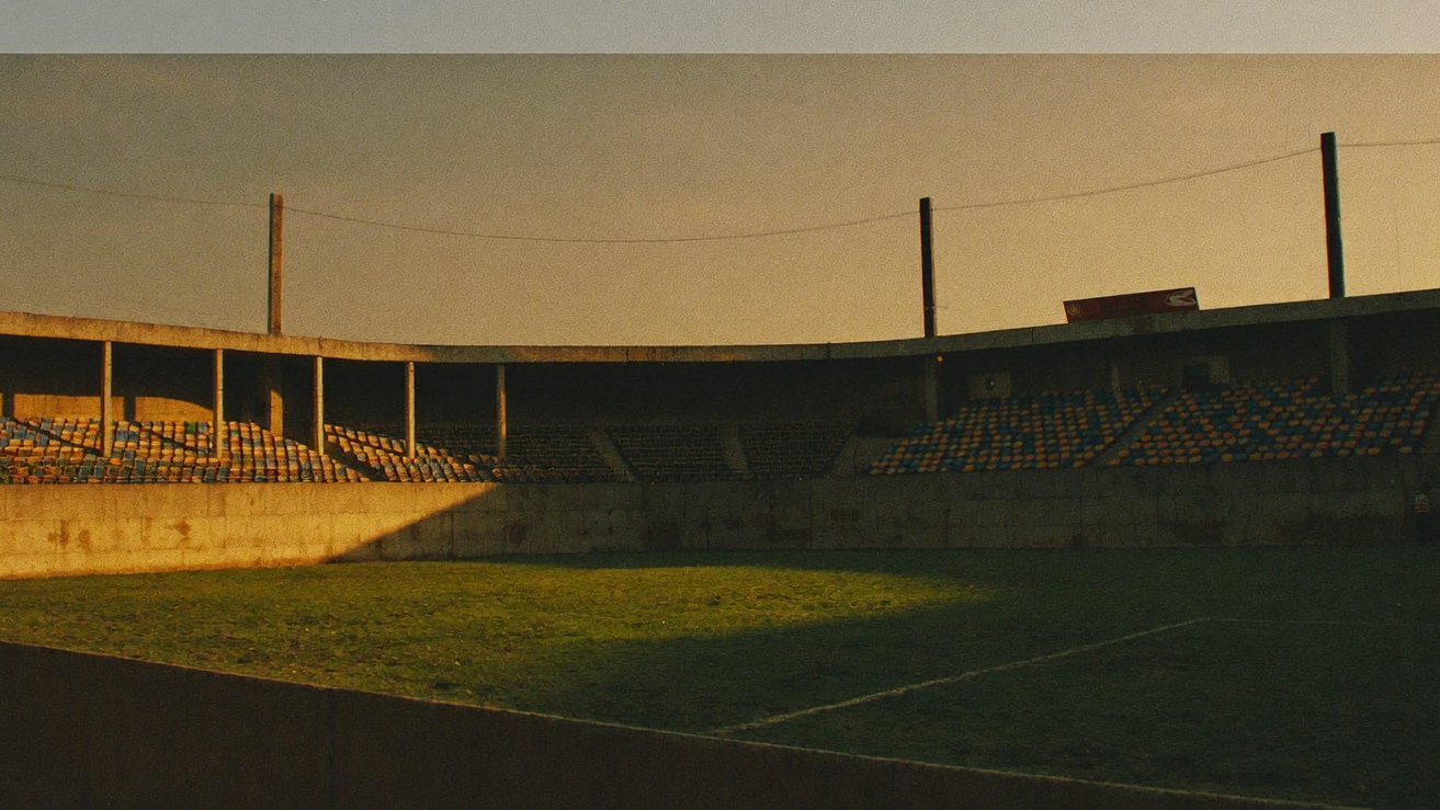 Estadio modesto sudamericano al atardecer con tribunas vacías